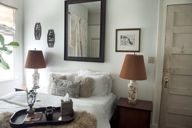 bedroom with two brown lamps and a white bed with pillows and a black framed mirror above