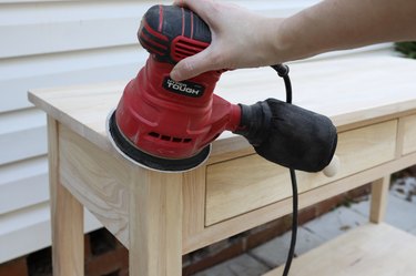 Sanding the corner of a wood table with an orbital sander
