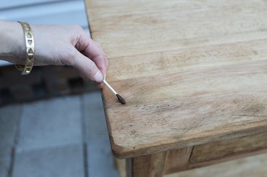pushing dark antiquing wax into holes in the table with a cotton swab