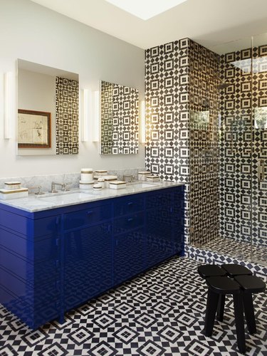 Modern bathroom with pattern tile floors and shower, blue vanity, mirror, stool.