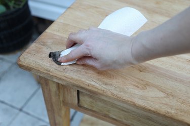 Applying dark antiquing wax to wood table with a white cloth