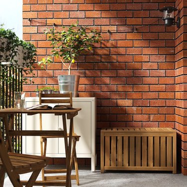 A wooden storage box from IKEA next to a wooden table and white cabinet in front of a brick wall.