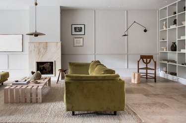 A living room with a travertine fireplace and velvet moss green sofa.