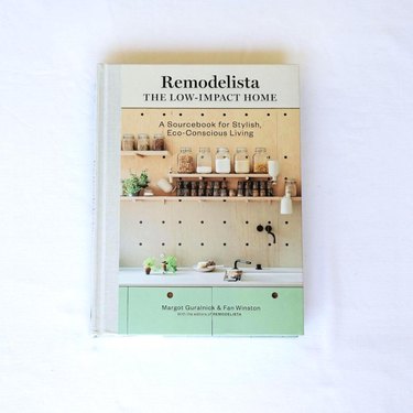 Book "Remodelista: The Low-Impact Home: A Sourcebook for Stylish, Eco-Conscious Living" placed on a white surface.