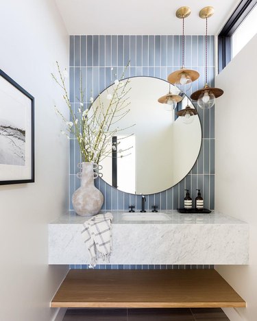 Small powder room space with mirror against blue tiles and above a marble sink