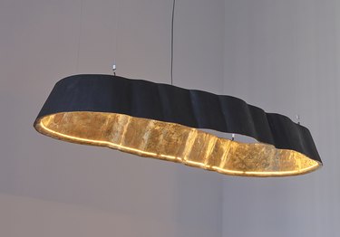 An oblong light pendant featuring a curved black metal outside and gold inside that reflects the light bulb.