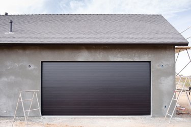 Gray roof house with a large black garage door and construction ladders