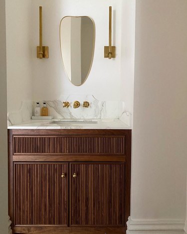 Small powder room with vintage mirror, custom vanity and slim, gold wall lights