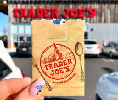 Hand holding a Trader Joe's gift card in front of a storefront