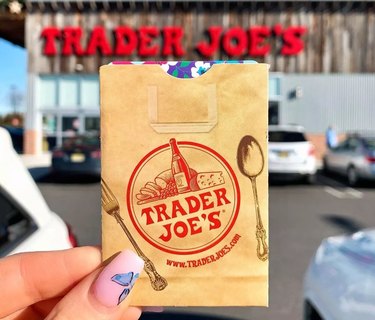 Hand holding a Trader Joe's membership card in front of a storefront