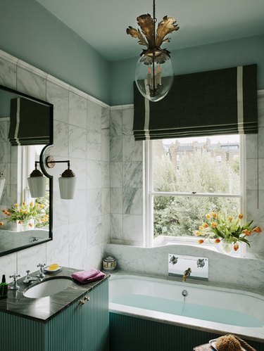 Traditional bathroom with white marble and blue-green paint, Dodo Egg lantern light fixture by Beata Heuman, and black bathtub