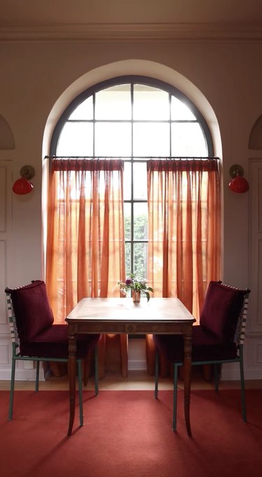 Table and chairs, burgundy rug, orange curtains.