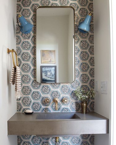 Bathroom with terra cotta tile backsplash, brass faucet, blue sconces, striped towel
