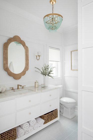 Modern luxe coastal white bathroom with light wood scalloped vanity mirror and sea glass beaded chandelier