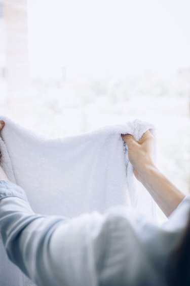 Hand fluffing white towel against white curtains