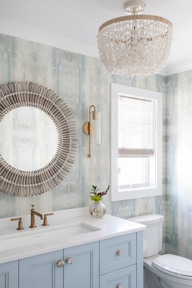 Costal bathroom with shell chandelier and blue cabinets.