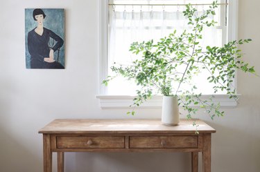Distressed wood table with an oil painting and vase of tall green leaves