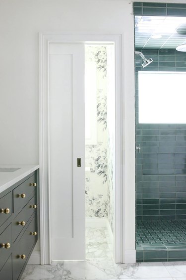 A white pocket door in a bathroom with green subway tile and a green vanity