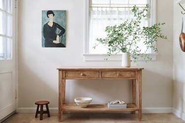 Distressed wood table in kitchen with an oil painting and vase of tall green leaves