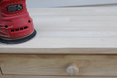 Sanding the edge of a wood table with an orbital sander