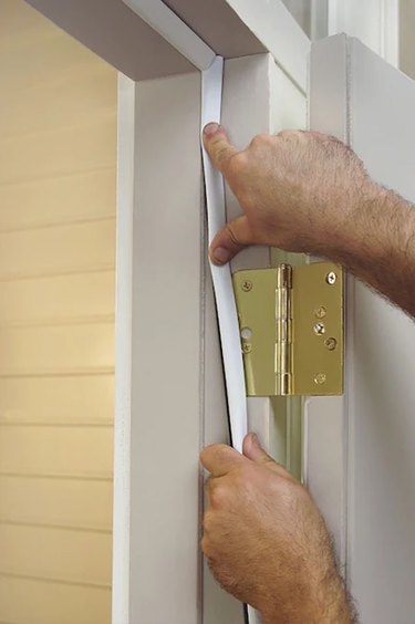 A white man's hands install weatherstripping on a white door