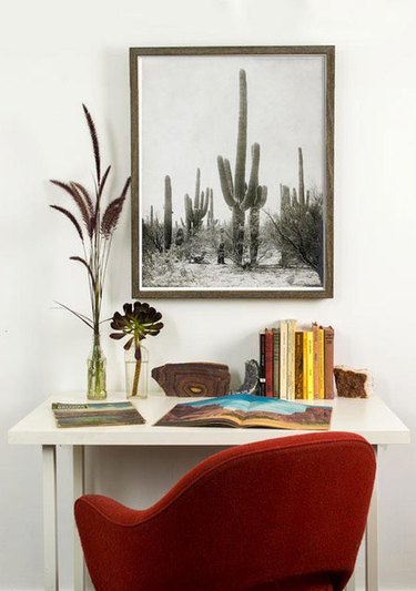 white desert style home office with red desk chair and large cactus print hanging above the desk