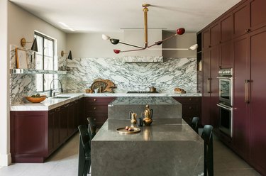 kitchen with maroon cabinets, taupe-colored stone island, marbled backsplash, and beige walls