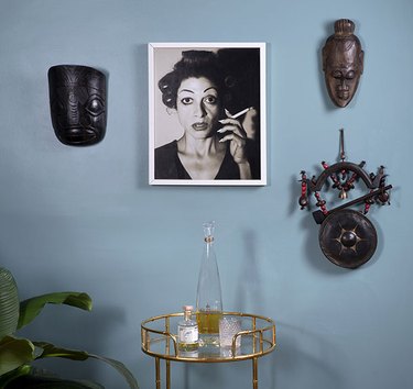 Baby blue wall with photograph and masks in Monica Orozco's living room