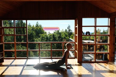 person doing yoga in room with large windows and solar light on the window