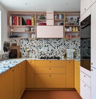 Kitchen with orange cabinets, terrazzo backsplash and counter, black stainless oven.