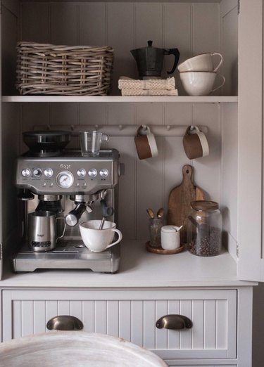 Gray kitchen cabinets with coffee maker, basket, mugs.