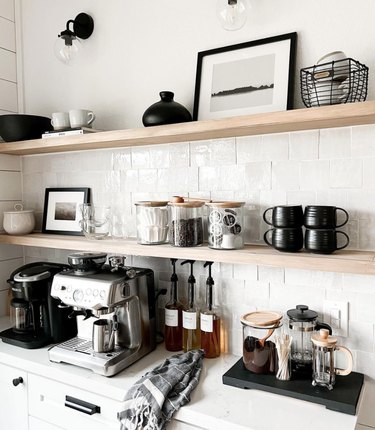 Kitchen counter with shelves, coffee makers, glassware, pottery.