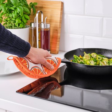 person at stove with orange-patterned pot holder and skillet with food