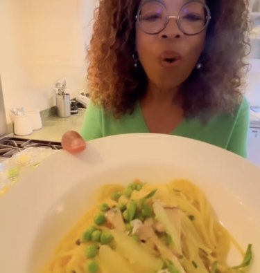 Oprah holds a dish of pasta with peas and mushrooms.