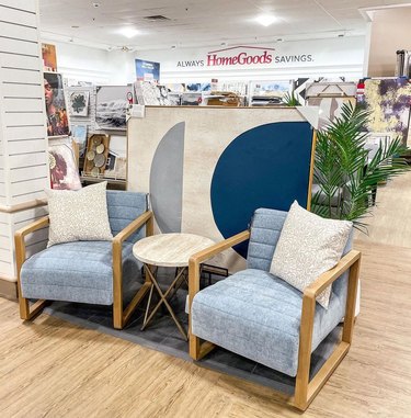 The inside of a HomeGoods store with two blue chairs and a light wood side table between them.