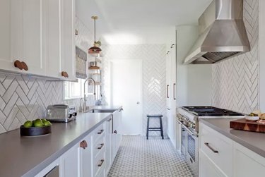 Kitchen with white cabinets, herringbone backsplash, tile floors.