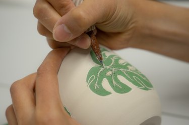 person painting leaf on ceramic piece