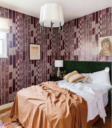 Bedroom with maroon wallpaper and orange bedding.