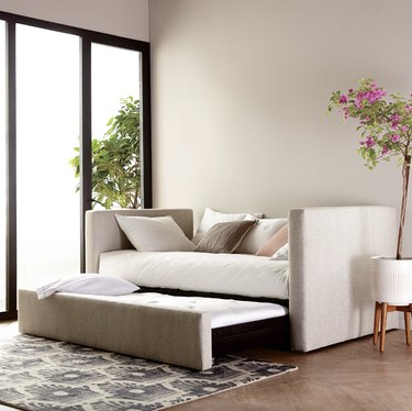 West Elm day bed with a trundle in a bedroom with a run and a floor-to-ceiling window