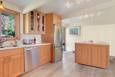 Kitchen with bamboo cabinets, track lighting, wood floors, stainless appliances.