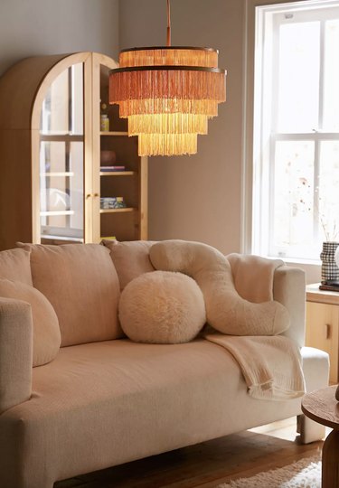 Urban Outfitters tiered fringe chandelier lit and hanging over a white sofa