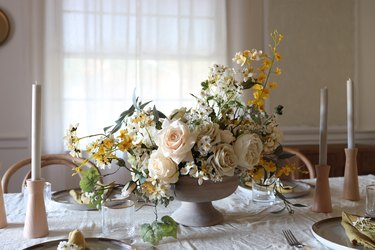 DIY faux spring centerpiece with white and yellow flowers on table with candles