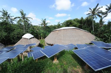 Solar panels next to two structures with grasslike domed roofs in the middle of a forest.