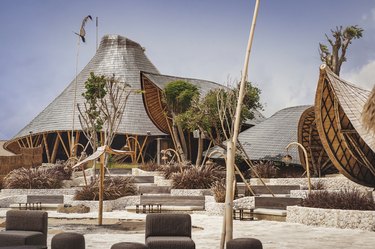 A beach club with bamboo buildings and long, sloping roofs.