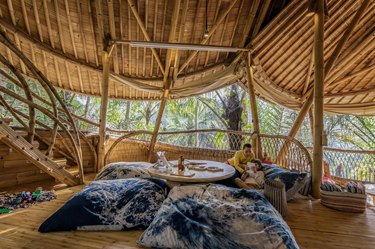 A bedroom in a building made from bamboo with two people lounging on blue and white speckled sheets on the bed.