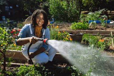 Loam Candles founder Jessica White, a woman with short black hair, watering a garden bed in a community garden.