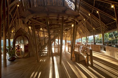 The interior of a building made from bamboo with light shining through the roof's slats onto the floor.