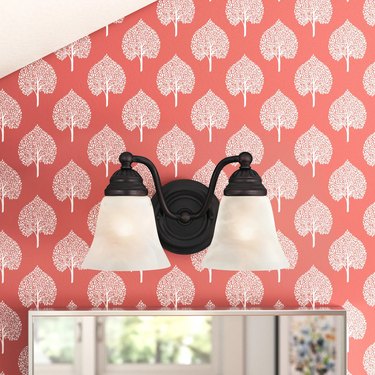 Bathroom with coral and white leaf patterned wallpaper and oil-rubbed bronze light fixture above mirror