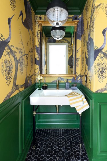 Bathroom with green wainscoting and yellow graphic wallpaper.