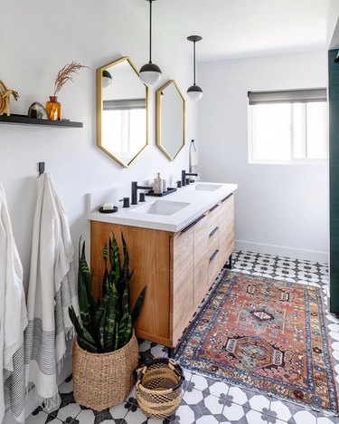 Boho bathroom with black and white mosaic tile, gold hex mirrors a Persian rug and floor baskets